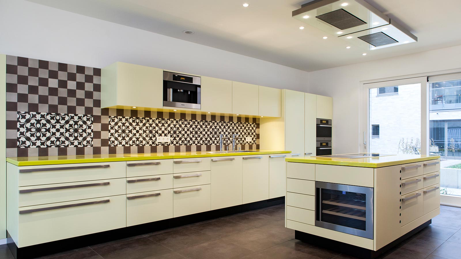 Diese originelle, von uns entworfene Küche mit emaillierter gelber Basalt Arbeitsplatte und Zementfliesen an der Rückwand hat einen Mittelblock mit Induktionskochfeld und Teppanyaki sowie einem Weinkühlschrank